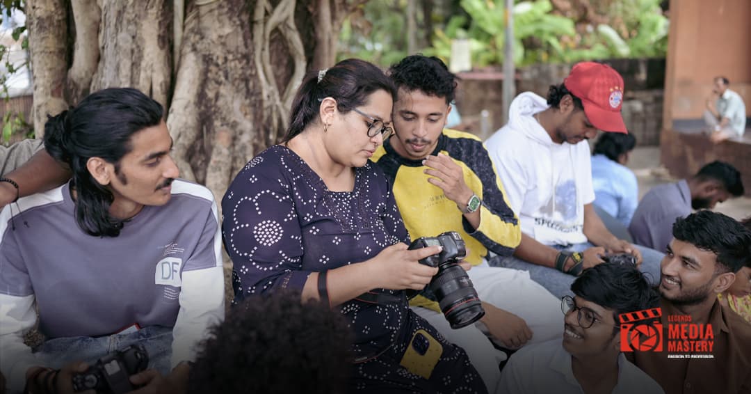 Instructor reviewing camera work with students under a tree during a photography class
