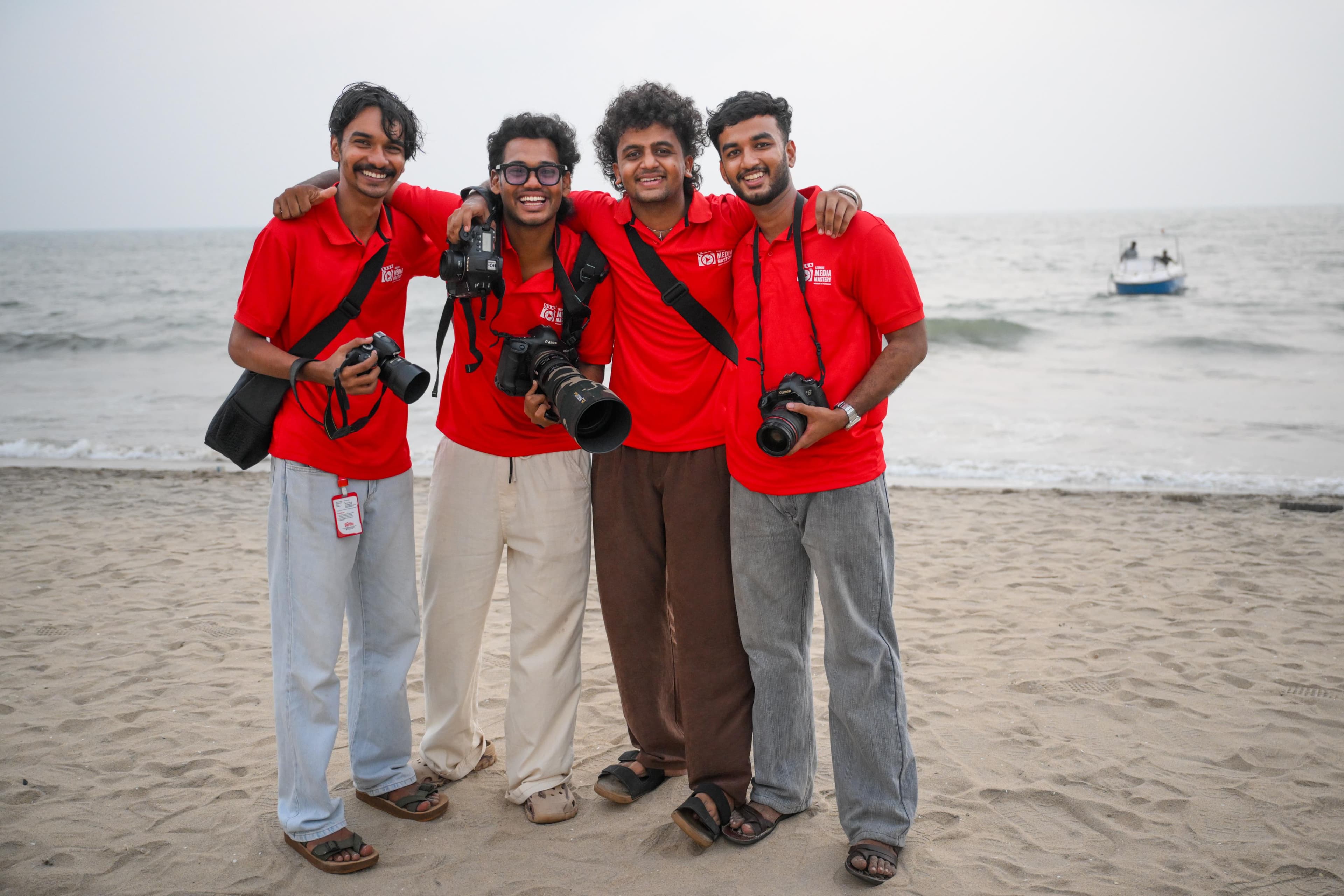 LMM batch of students in red jerseys with cameras at a Kerala beach – group photo