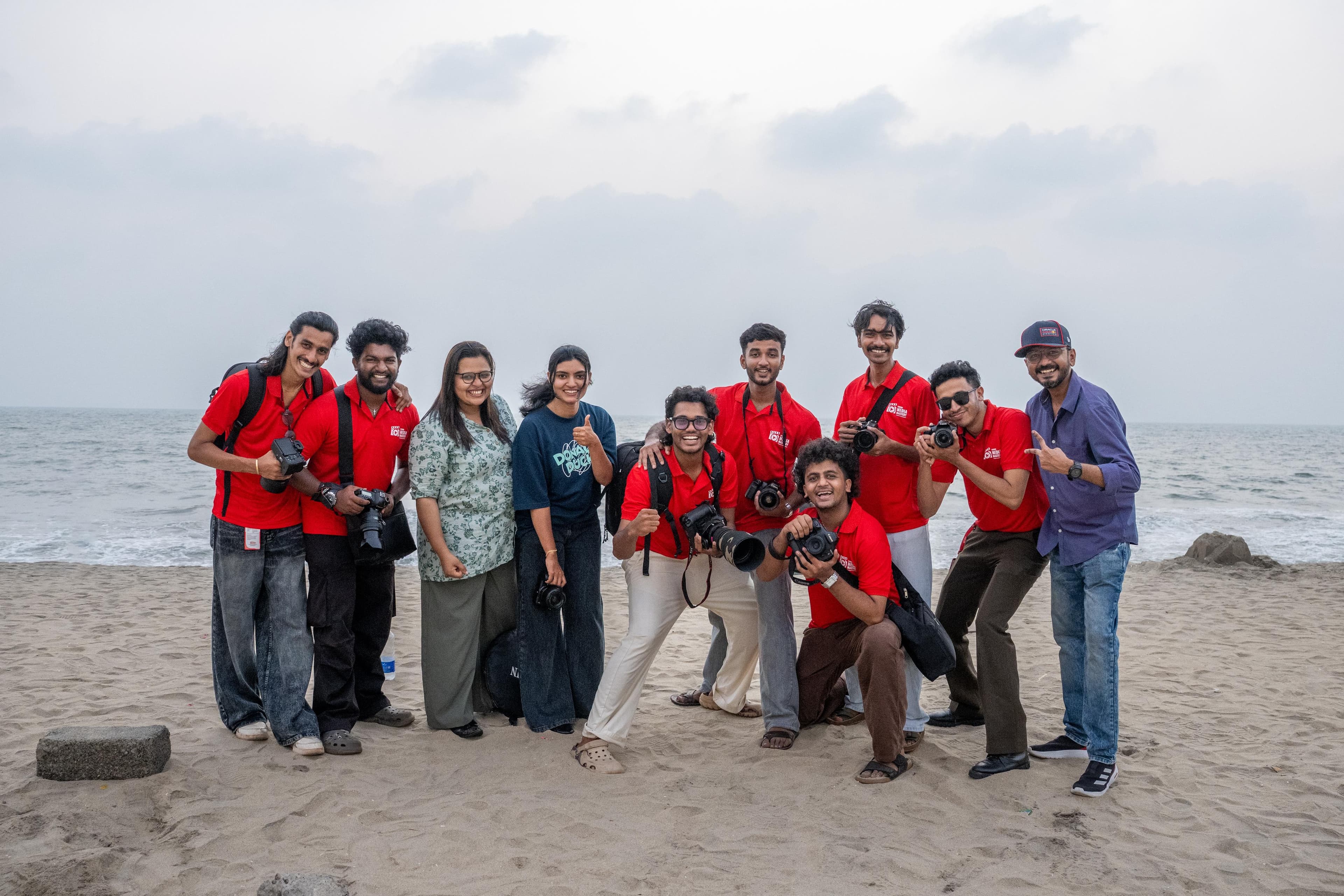 Large group of Legends Media Mastery students celebrating at the beach with cameras